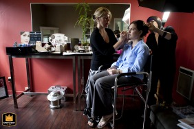 Inside the MacCallum House in Mendocino, California, the bride sits quietly as her makeup is delicately applied, surrounded by rich burgundy walls and warm wood floors, creating an atmosphere of elegance and anticipation before the ceremony.
